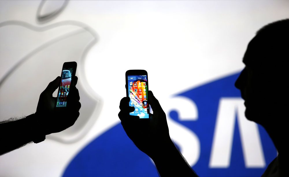 Men are silhouetted against a video screen with Apple and Samsung logos as he poses with Samsung S3 and Samsung S4 smartphones in this photo illustration taken in the central Bosnian town of Zenica