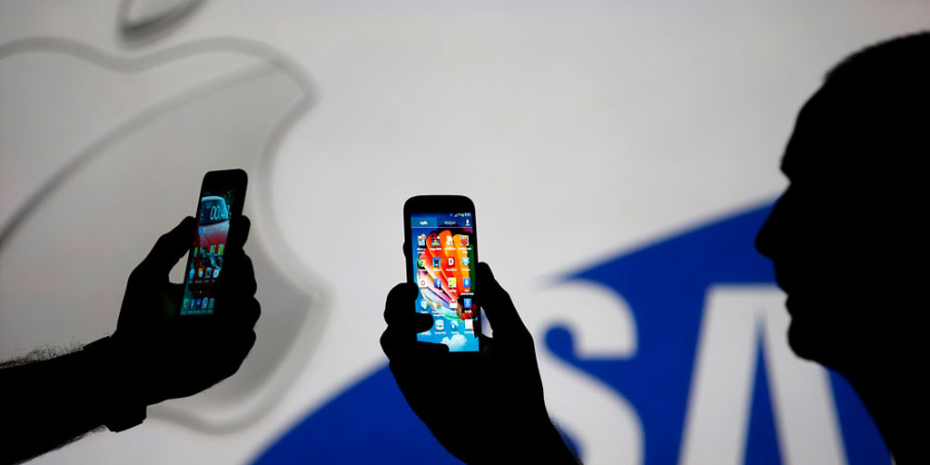 Men are silhouetted against a video screen with Apple and Samsung logos as he poses with Samsung S3 and Samsung S4 smartphones in this photo illustration taken in the central Bosnian town of Zenica, August 14, 2013. REUTERS/Dado Ruvic (BOSNIA AND HERZEGOVINA - Tags: BUSINESS TELECOMS) - RTX12L6W