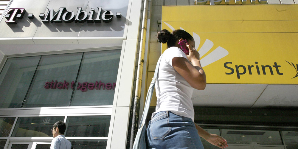 A woman talks on her phone as she walks past T-mobile and Sprint wireless stores in New York in this file photo from July 30, 2009. Sprint Corp is mulling a bid for T-Mobile US, according to a report in the Wall Street Journal citing people familiar with the matter. REUTERS/Brendan McDermid/Files (UNITED STATES - Tags: BUSINESS TELECOMS)