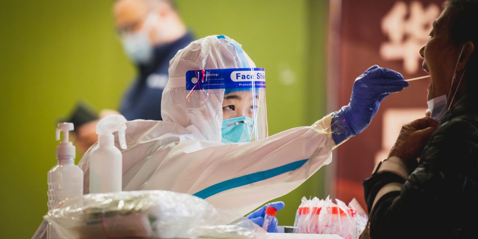 Health worker in protective kit performing a swab test | Apple production halted at three key Chinese suppliers