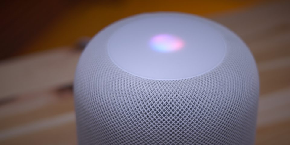 White HomePod on table with Siri light lit up.