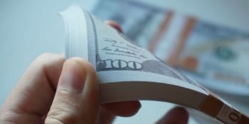 Apple was fined $2.1B last year, but could pay it all off in a week | Close-up of a hand flicking through a stack of $100 bills