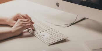 Attacker used ChatGPT to trick Mac users into installing MacStealer | A close-up photo of fingers typing on a Magic Keyboard attached to an iMac